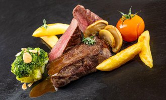 Ein saftiges Steak mit Röstaromen, serviert mit Pommes Frites, Brokkoli und einer Tomate. Das Gericht wird von Kräutern und Champignons begleitet. | © Hotel Alte Krone