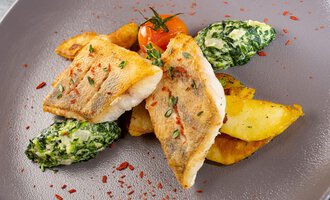 Ein Teller mit gebratenem Fischfilet, knusprigen Kartoffeln und gedünstetem Spinat. Frische Tomaten und Gewürze sorgen für einen ansprechenden Look. | © Hotel Alte Krone